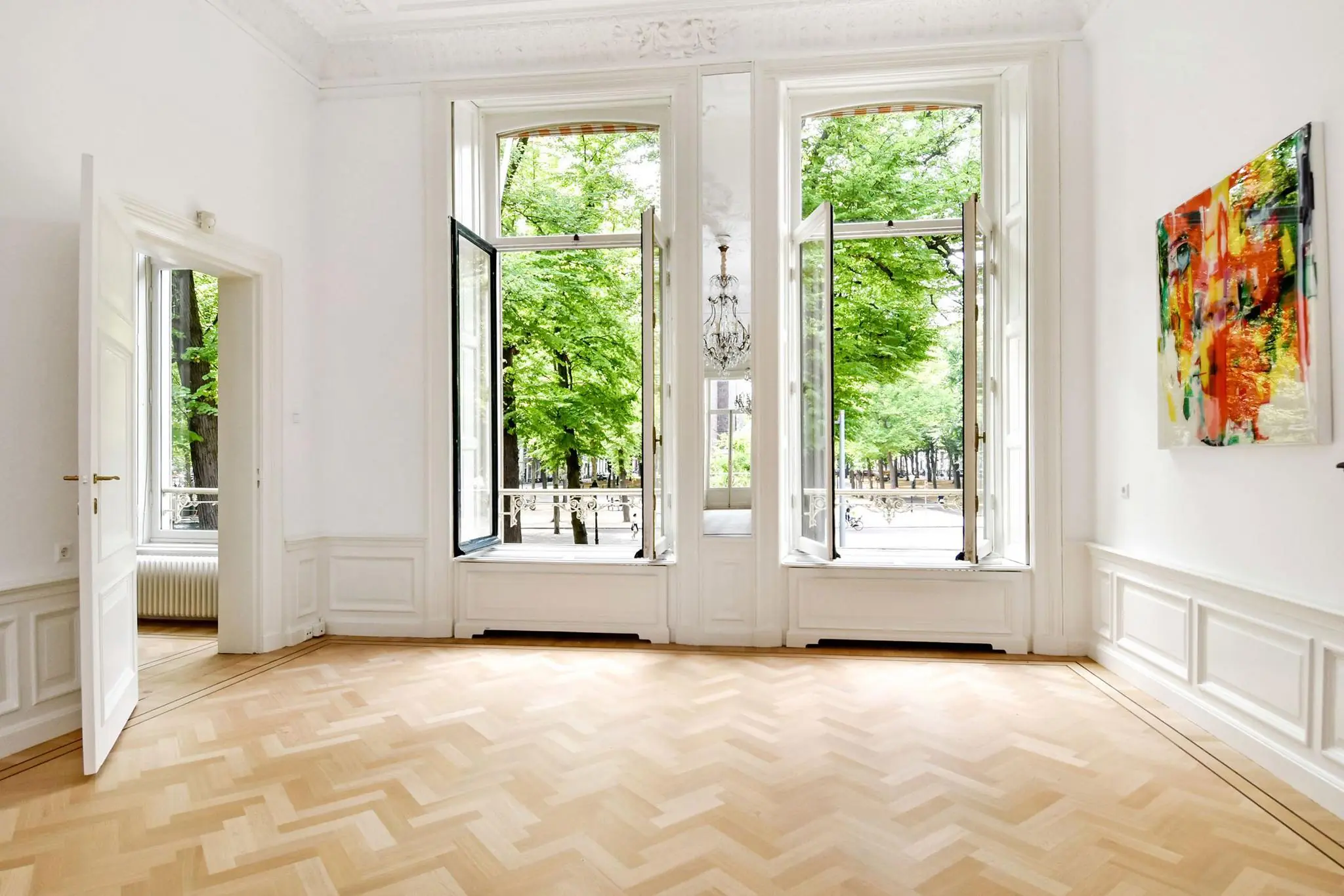 Lichte, klassiek ingerichte kamer met visgraatparket en uitzicht op de groene bomen aan het Lange Voorhout in Den Haag.